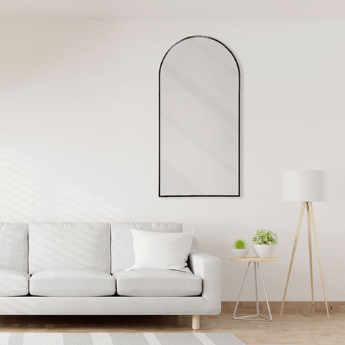 Arched wall mirror with black frame styled above a sofa in a living room